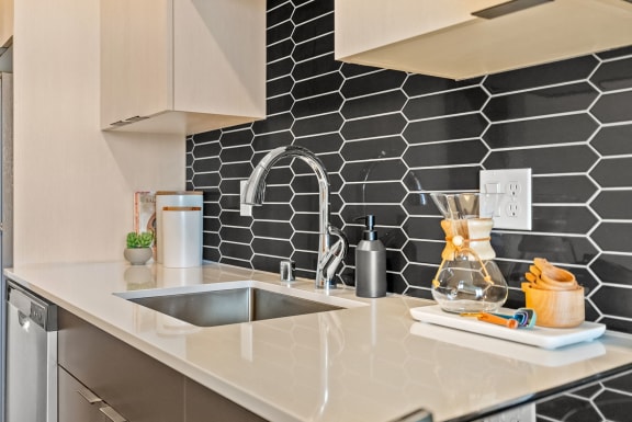 a kitchen counter with a sink and black tile walls at Hue Apartments, Redmond, WA