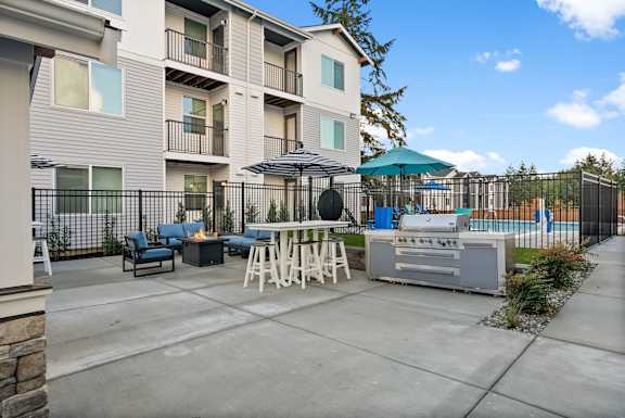 A patio area with a grill and seating area in front of a building.