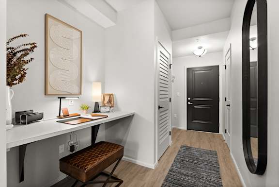 A white desk with a brown stool and a framed picture on the wall.
