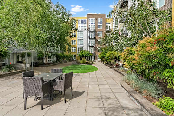 A patio with a table and chairs is surrounded by greenery and apartment buildings.