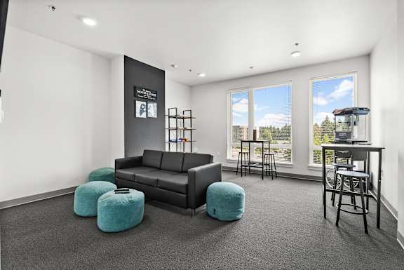 A black couch with a blue ottoman in front of a window.