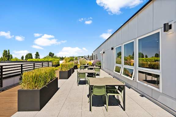 A patio with a table and chairs is surrounded by a white building and a railing.