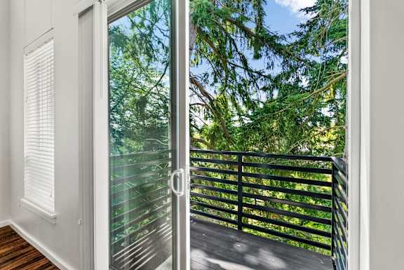A glass door with a handle is open to a balcony with a black railing.