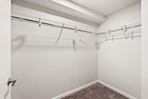 A white closet with a carpeted floor and metal hangers.