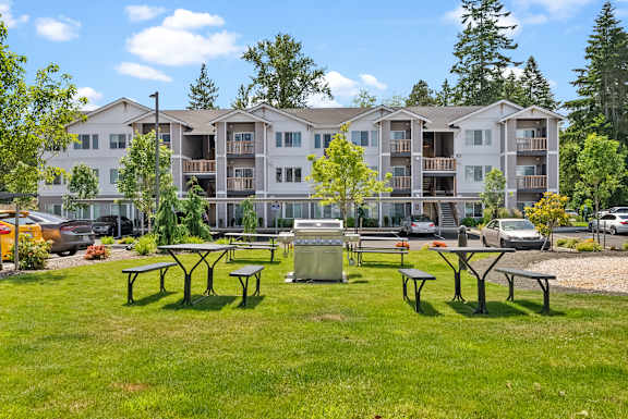 A grassy area with picnic tables in front of apartment buildings.