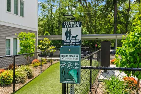 A sign for a dog waste station is posted on a fence.
