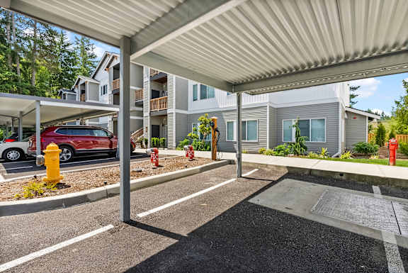 A parking lot with a red car and a white van under a canopy.