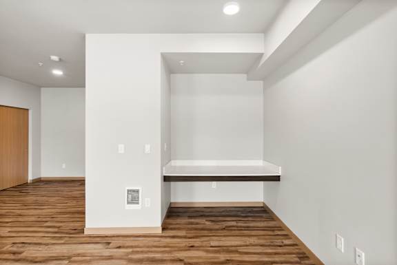 A room with a wooden floor and a white wall with a shelf and a door.