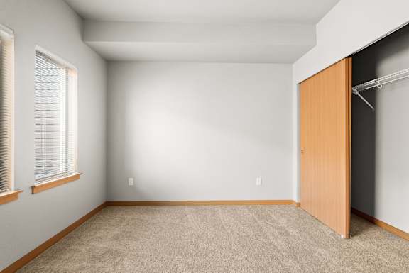 A room with a carpeted floor, a wooden door, and a window with blinds.