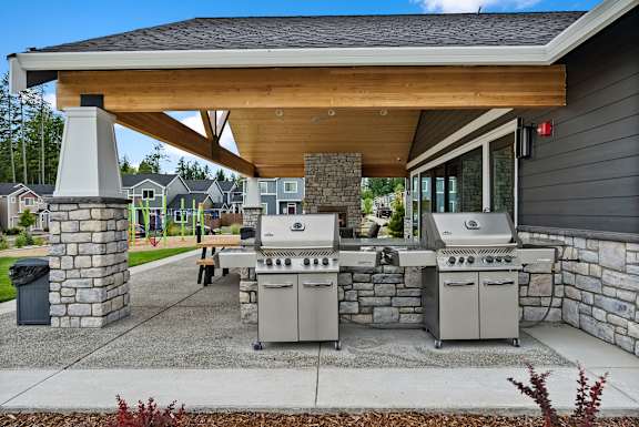 A covered outdoor kitchen area with grills and a table.