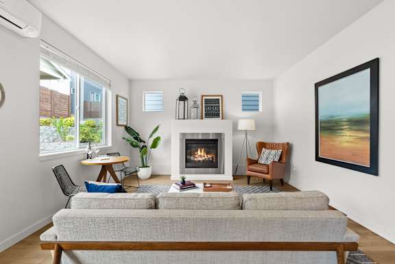 A living room with a grey couch, a fireplace, and a painting on the wall.
