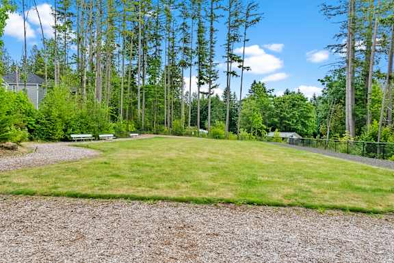 A gravel area in the foreground with a grassy area and trees in the background.