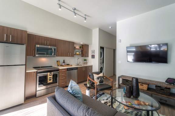 A modern kitchen with a grey couch and a glass table.