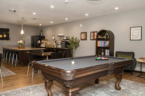 A pool table is in the middle of a room with a bar and a dining table.