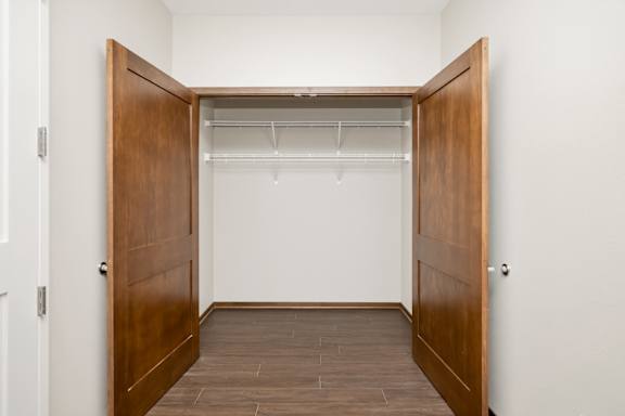 A room with a wooden floor and a closet with a white shelf.