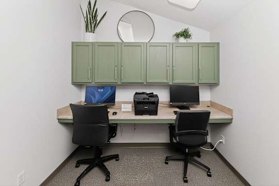 A small office with a desk, two chairs, and a plant on the shelf.