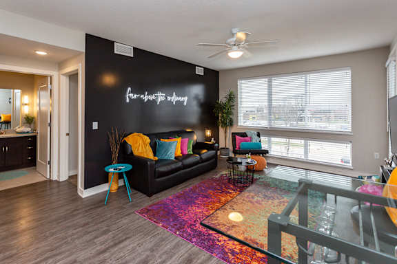 A living room with a black couch and a neon sign on the wall.