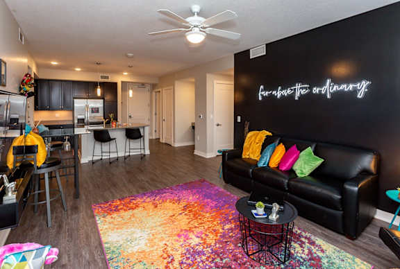 A living room with a black couch and a colorful rug.