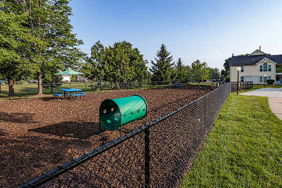 A green barrel sits on a chain link fence in a park.