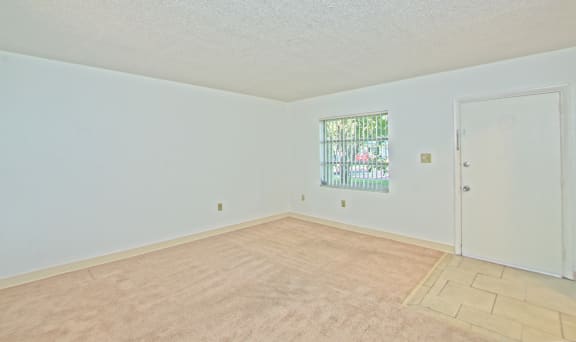 the spacious living room of an empty home with white walls and carpet