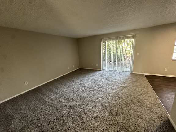 A room with a carpeted floor and a sliding glass door.at Auburn Glen Apartments, Jacksonville