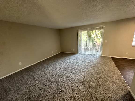 A room with a carpeted floor and a sliding glass door leading outside.at Auburn Glen Apartments, Jacksonville
