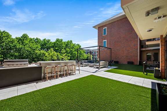 A patio area with a table and chairs is surrounded by a grassy area and a brick building.