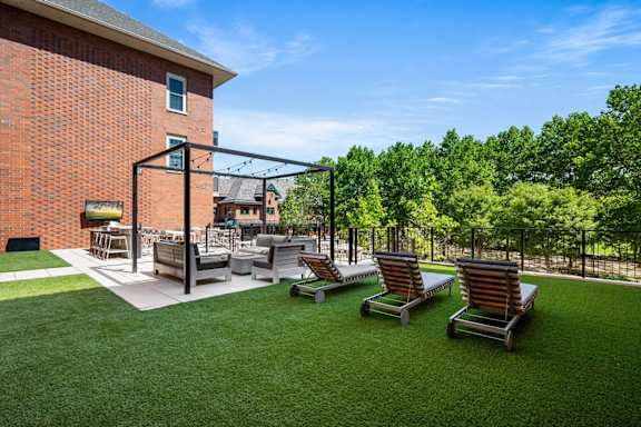 A patio area with a lawn, chairs, and a building in the background.