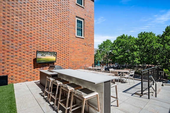 A patio with a bar and chairs is set against a red brick wall.