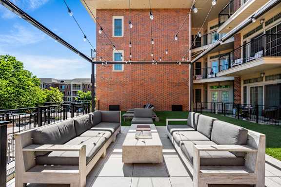 A patio with a table and couches with a brick building in the background.