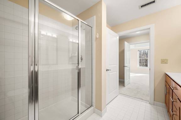 A bathroom with a glass shower door and a white tiled floor.