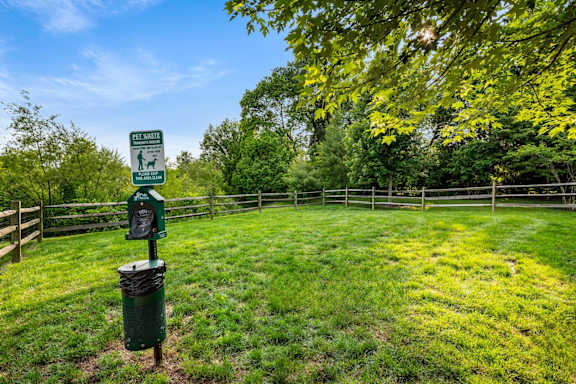 A sign for a dog park is in the foreground of a grassy area.