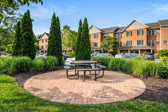 A brick patio with a table and chairs in the middle of a grassy area.