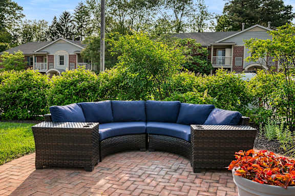 A blue wicker sofa set on a brick patio with a bowl of red flowers in front.