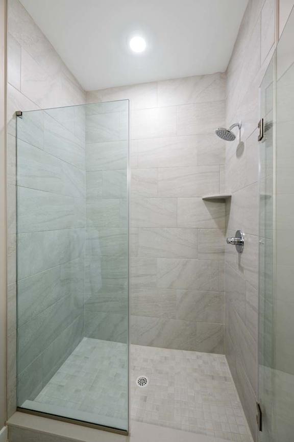A shower area with a glass door and a glass shelf.