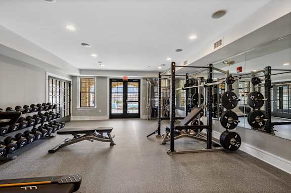 A gym with a variety of equipment including dumbbells, weight plates, and a bench press.
