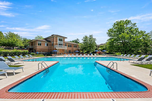 A large swimming pool with a red brick border and a building in the background.