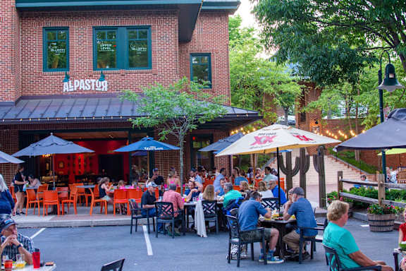 A group of people are sitting at tables outside of a restaurant named Al Pastor.