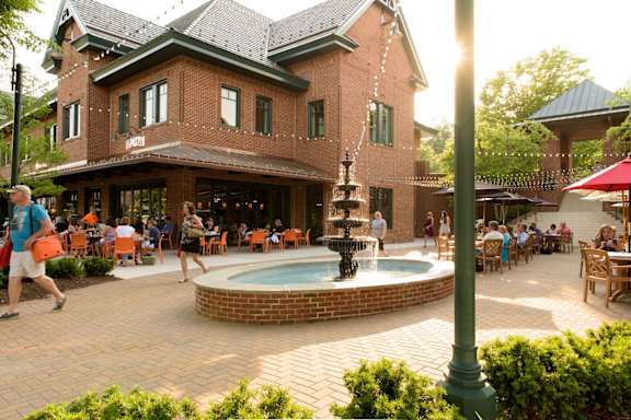A group of people are sitting at tables under umbrellas in a courtyard.
