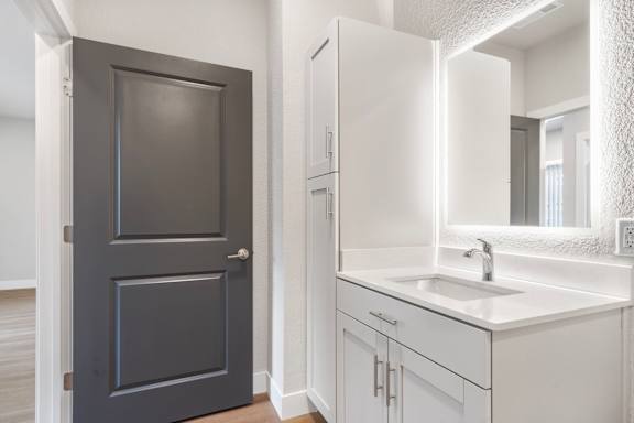 A bathroom with a sink, mirror, and a black door.