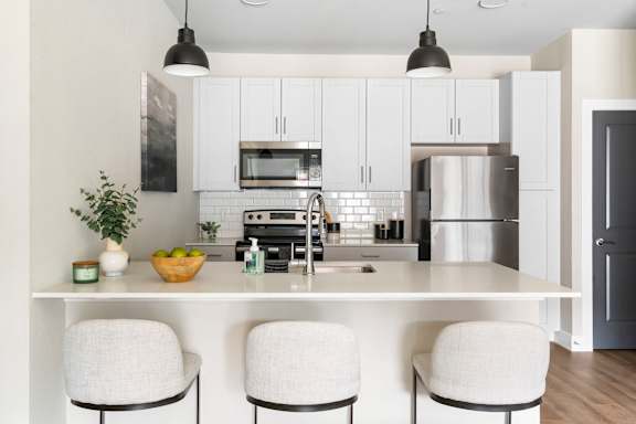A modern kitchen with white cabinets and a white island with three chairs.