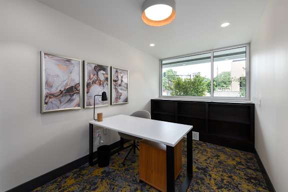 A white desk with a black chair in a room with a window.
