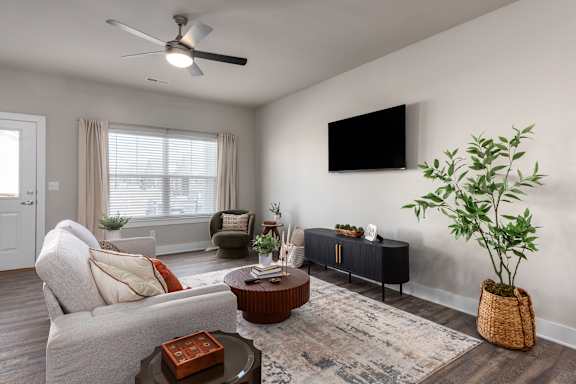 A living room with a grey couch, a brown coffee table, a TV on the wall, and a plant in a basket at Hawk Ridge Apartments, Lake St. Louis, MO, 63367