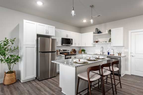 A kitchen with a refrigerator, microwave, and a counter with chairs at Hawk Ridge Apartments, Lake St. Louis, MO, 63367