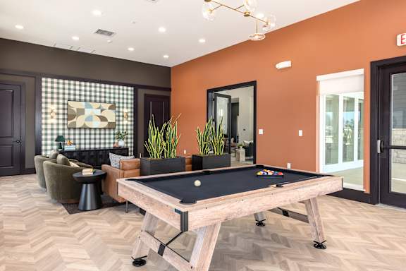 A pool table is in the middle of a room with a brown floor and orange walls at Hawk Ridge Apartments, MO, 63367