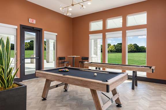 A pool table in a room with orange walls and a view of a green lawn outside the window at Hawk Ridge Apartments, Missouri, 63367