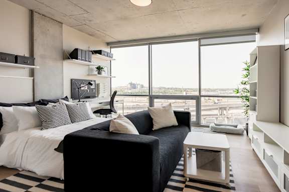 A black and white bedroom with a large window overlooking the city. at One Foundry Way Apartments, St Louis, 63110