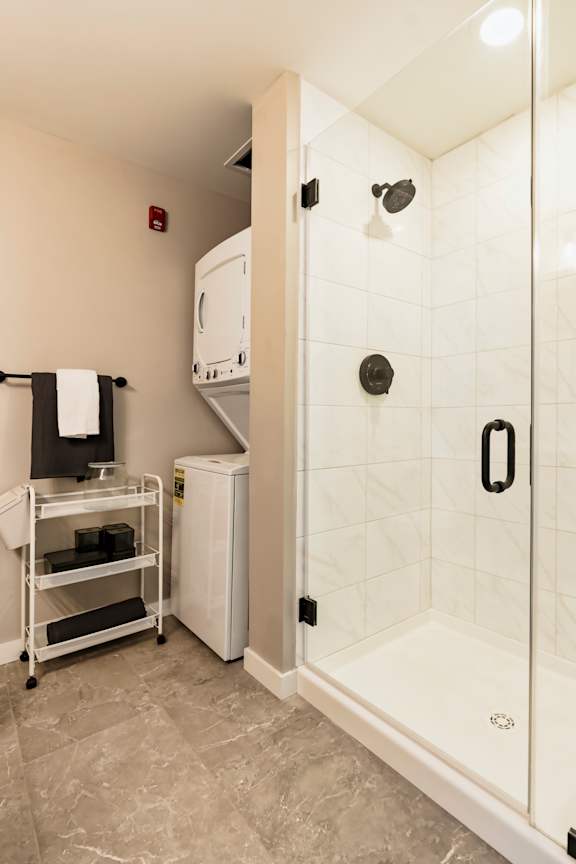 A white tiled shower with a black handle is on the right side of the image. at One Foundry Way Apartments, Missouri