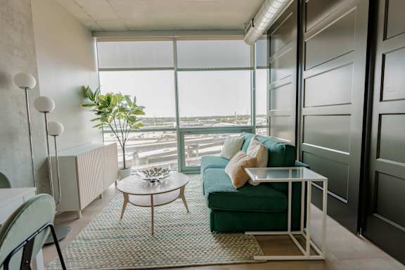 A living room with a green couch, a glass table, and a large window overlooking the city. at One Foundry Way Apartments, Missouri