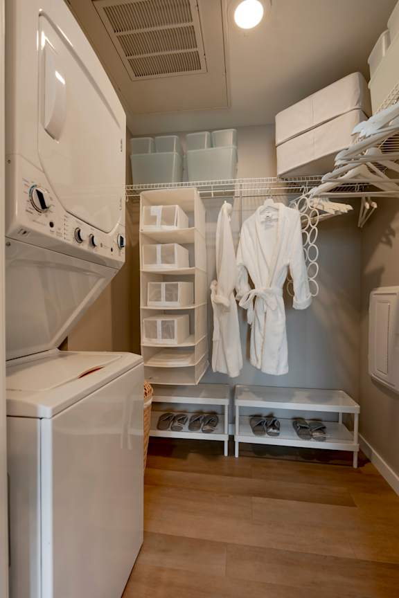 A laundry room with a washer and dryer and a rack of white robes. at One Foundry Way Apartments, St Louis, MO